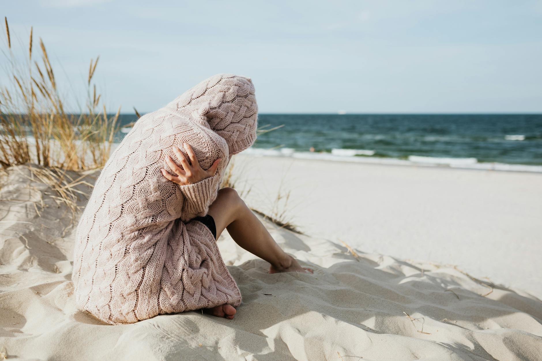 woman in pink knitted hoodie sitting on white sand