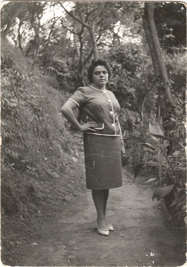 Donna in abiti vintage posando su un sentiero circondato da vegetazione.