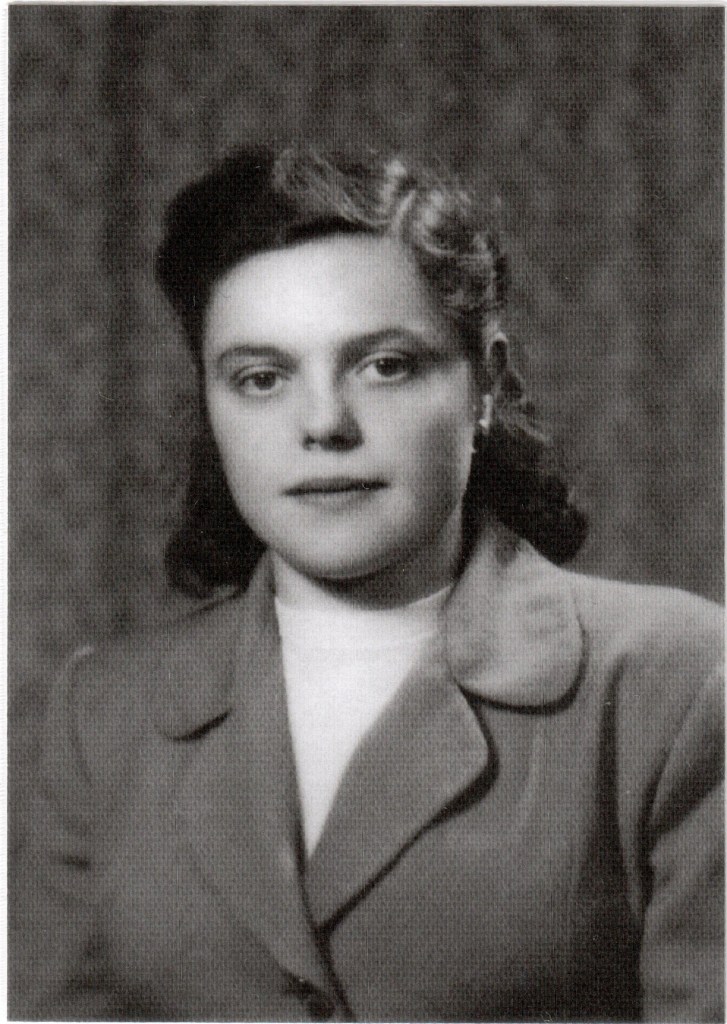 Ritratto in bianco e nero di una giovane donna con capelli ricci, vestita con giacca chiara e maglione bianco, in un ambiente scuro