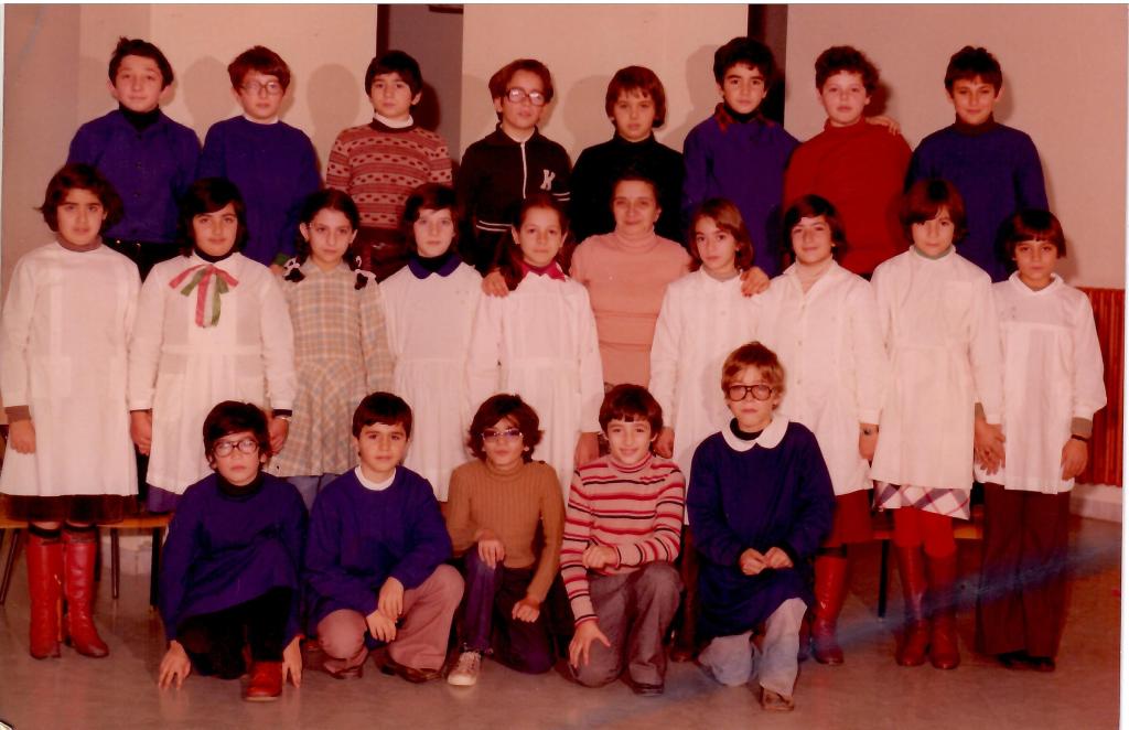 Gruppo di bambini e insegnanti in una scuola, con diversi stili di abbigliamento degli anni '70, posando per una foto di classe.