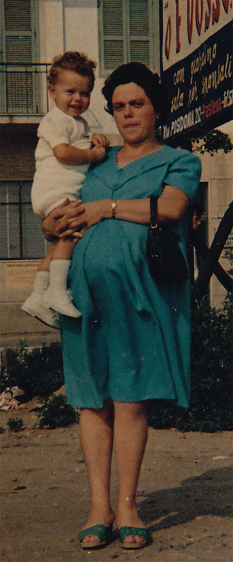 A woman in a turquoise dress holding a smiling toddler, standing outdoors with a sign in the background.
