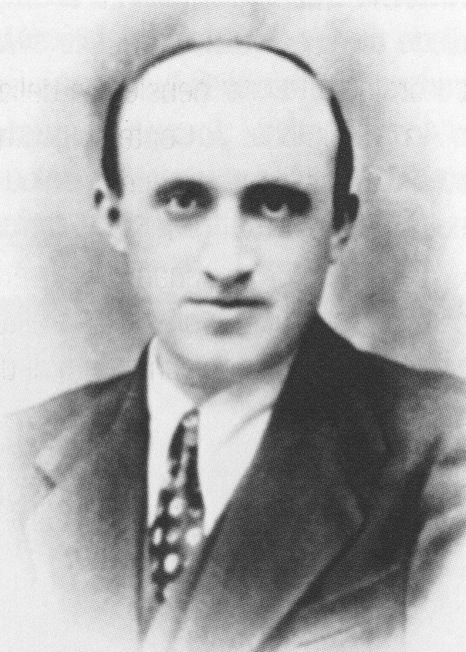 Ritratto in bianco e nero di un uomo con capelli radi, indossa una giacca e cravatta, con uno sfondo sfocato.