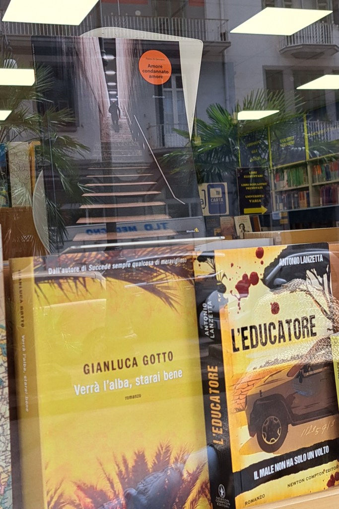 Vetrina di una libreria con diversi libri esposti, tra cui 'Amore condannato amore' di Pietro Di Gennaro, visibile in primo piano con un'etichetta arancione.