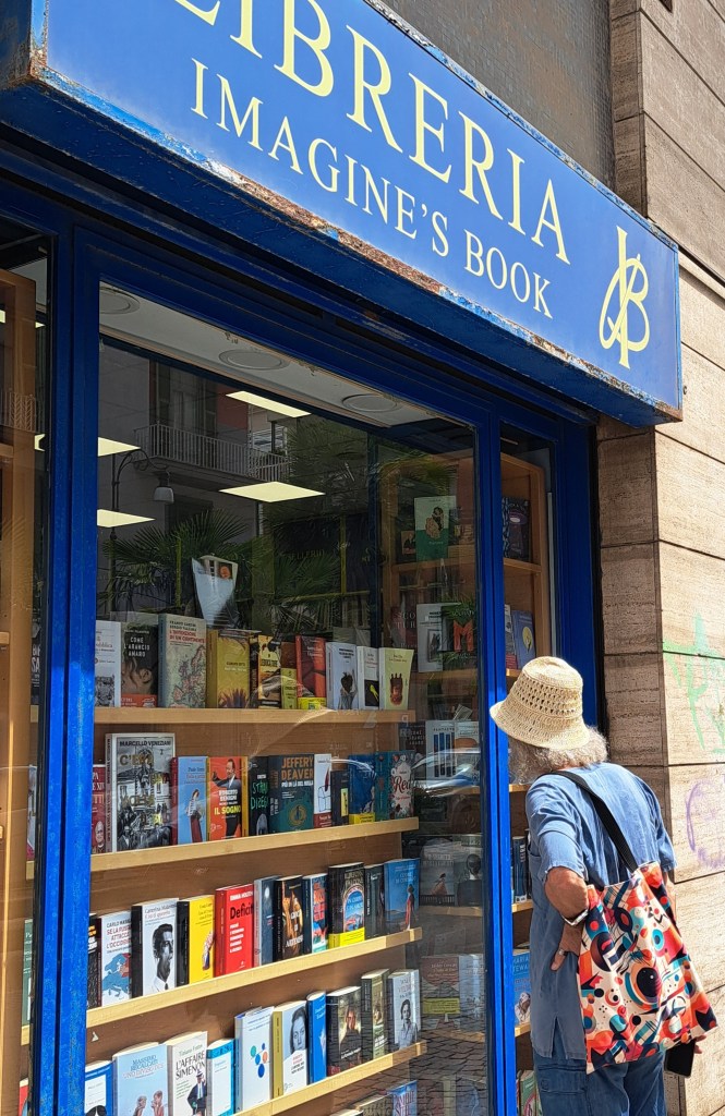 Una persona osserva le vetrine della libreria 'Imagine's Book', con molti libri esposti, in una giornata di sole.